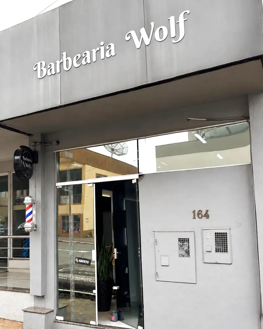 Fachada da Barbearia Wolf na Av. Brasil, 164, com o letreiro, o poste de barbeiro e a porta de vidro